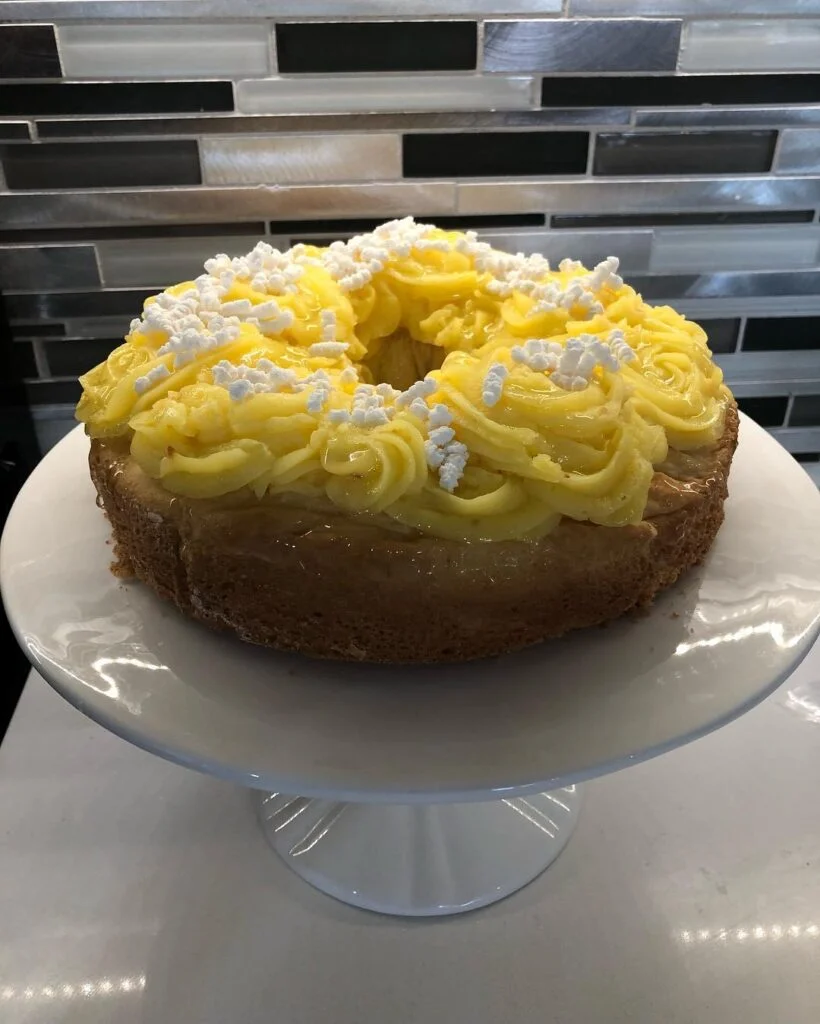 This is a photo of a three-tiered white wedding cake. The cake is decorated with large white flowers and green leaves. The flowers are orchids and they are arranged in a cascading manner. The cake is on a white cake stand.